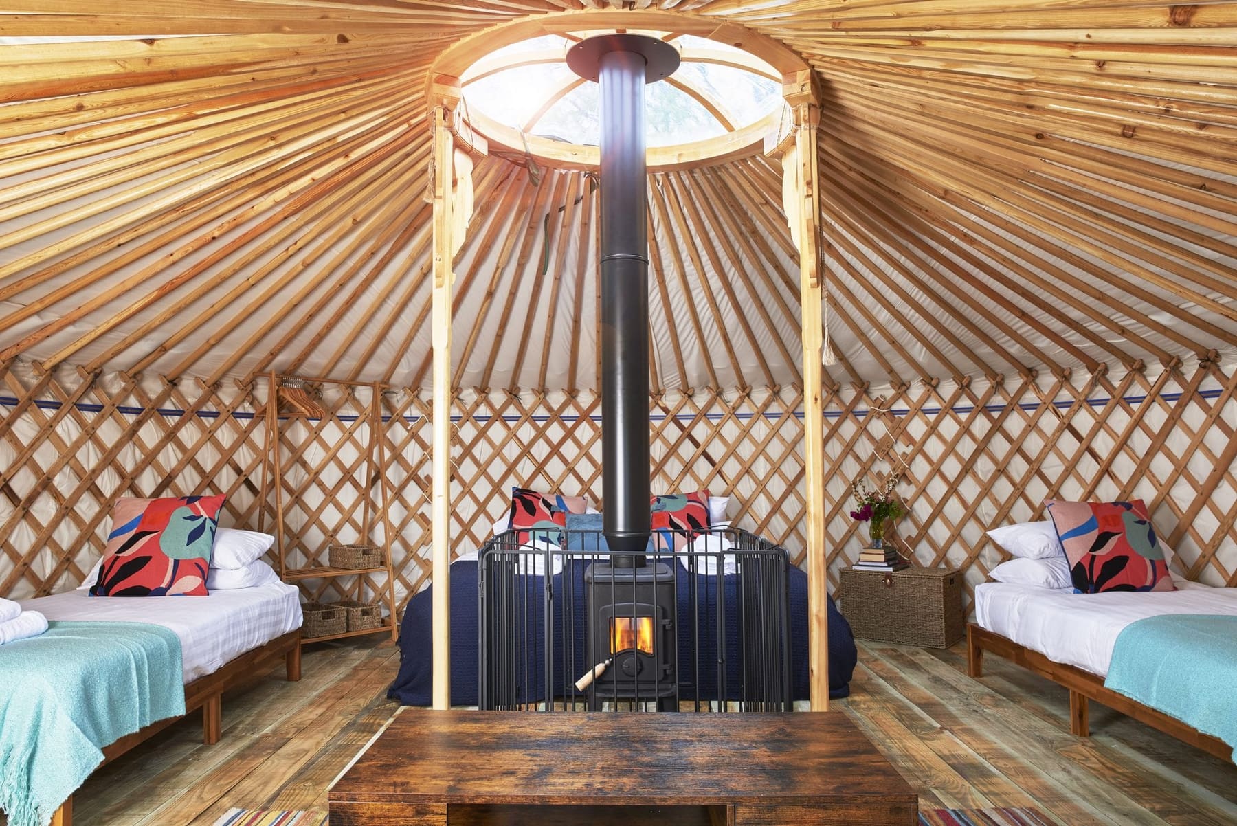 Inside Fenton yurt, wood burner beneath the crown skylight with a super-king and two single beds