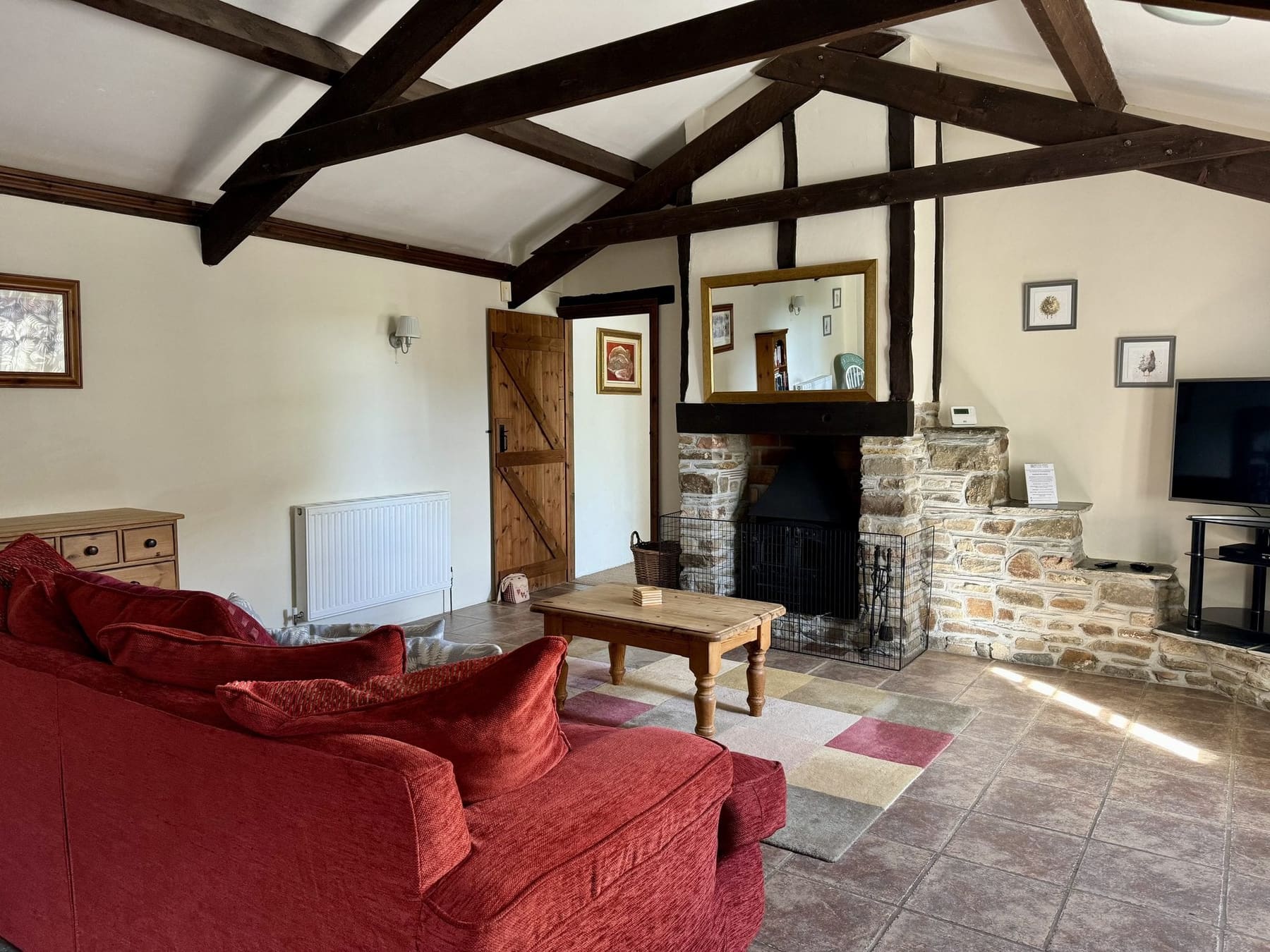 Honeysuckle Cottage lounge with red sofa beneath exposed beams